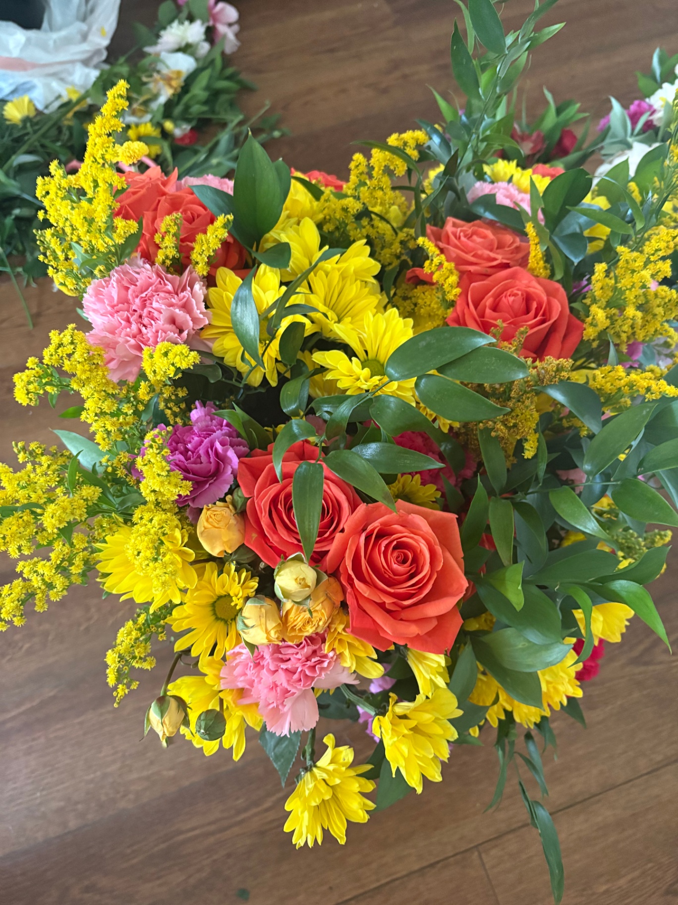 A volunteer arranging rescued flowers at a wooden workshop table